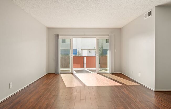 A room with a wooden floor and a glass door leading to a balcony.