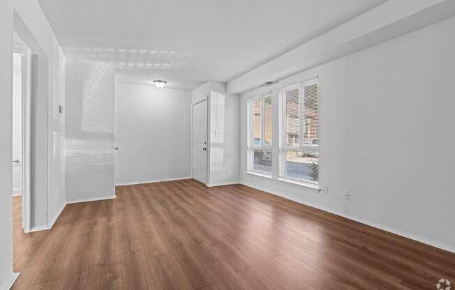 a living room with white walls and wood floors and a window