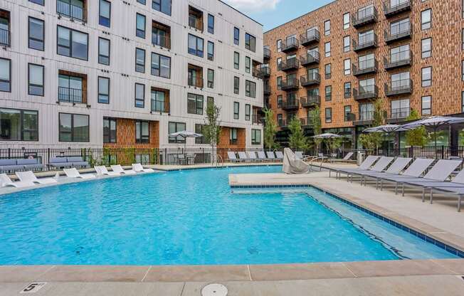 A large outdoor swimming pool surrounded by lounge chairs and buildings.