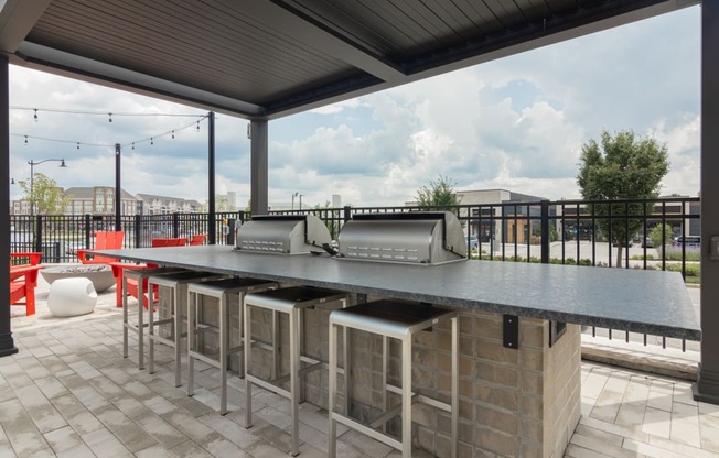 a bar area with a grill and chairs on a patio