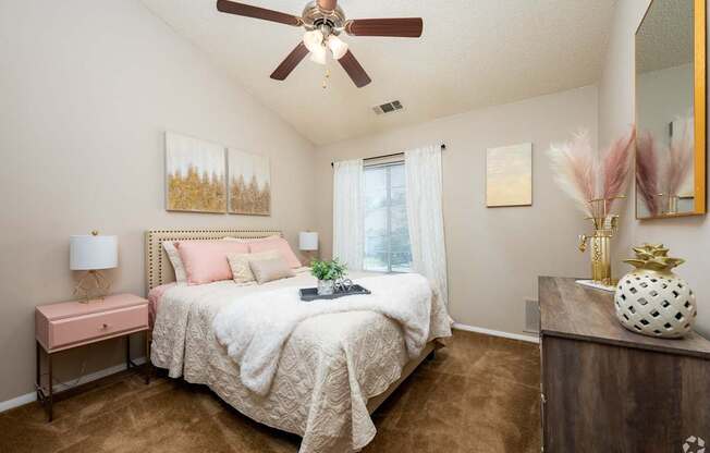 A bedroom with a bed, a pink table, and a ceiling fan.