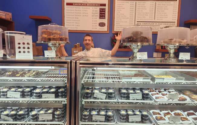 a man standing behind the counter of a display case of donuts