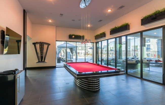 A game room with a red pool table and tv and glass windows and mini fridge