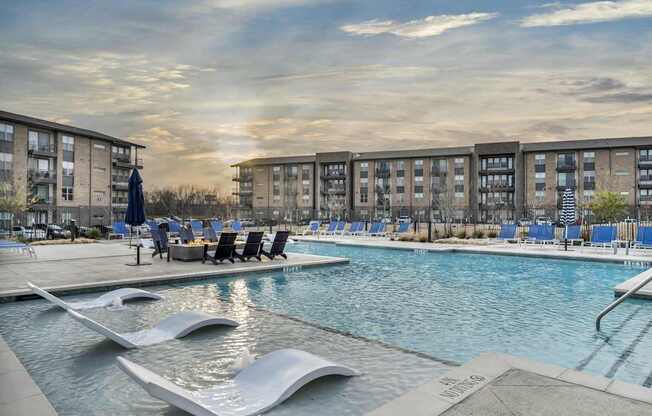 A swimming pool with a slide and loungers in front of apartment buildings.