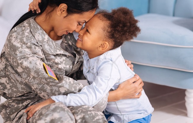 a woman in a military uniform is sitting on the floor and smiling at a little girl