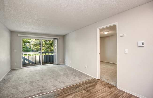 an empty living room with a sliding glass door to a balcony