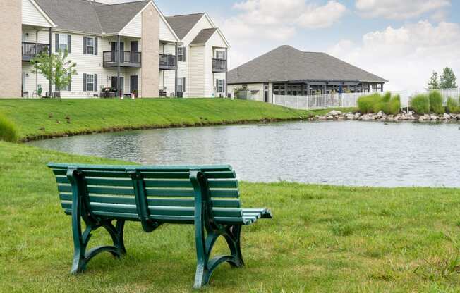 a park bench sits in front of a lake with apartment buildings in the background