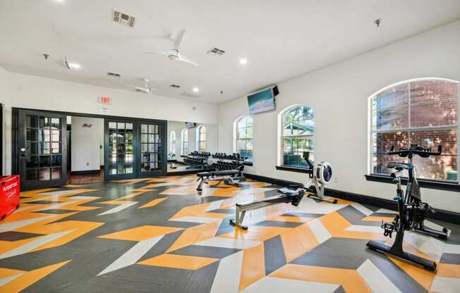 a gym with a colorful tile floor and bikes in a room with windows