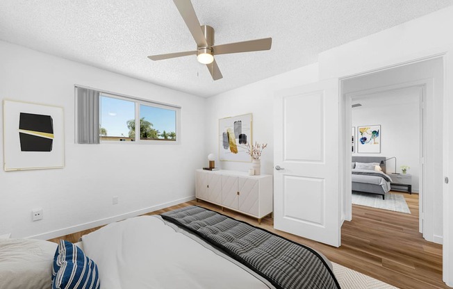A bedroom with a bed, a ceiling fan, and a window with a view of the outdoors.