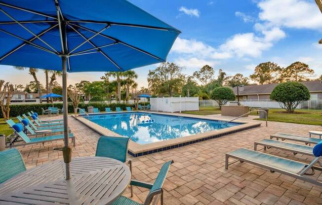 Swimming pool deck with blue lounge chairs and a table with umbrella