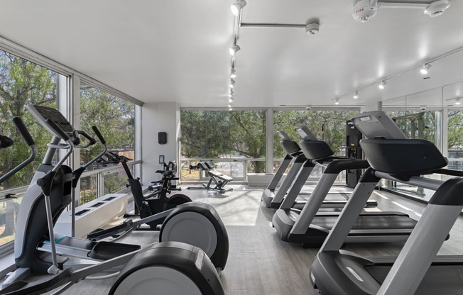 a gym with treadmills and other cardio equipment in a building with large windows