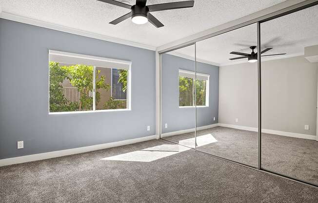 Carpeted bedroom with ceiling fan and large mirrored closet.