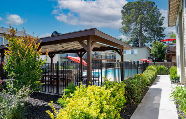 View into gated community pool with covered area that has a picnic table and seating areas, surrounded by lush landscaping