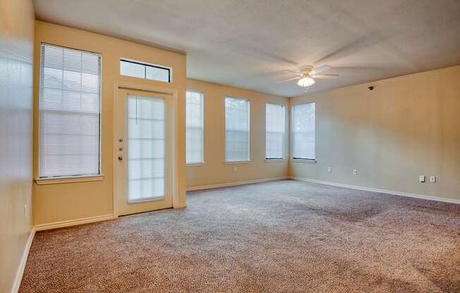 an empty living room with a ceiling fan and four windows