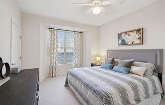 A bedroom with a bed, a ceiling fan, and a window with curtains.