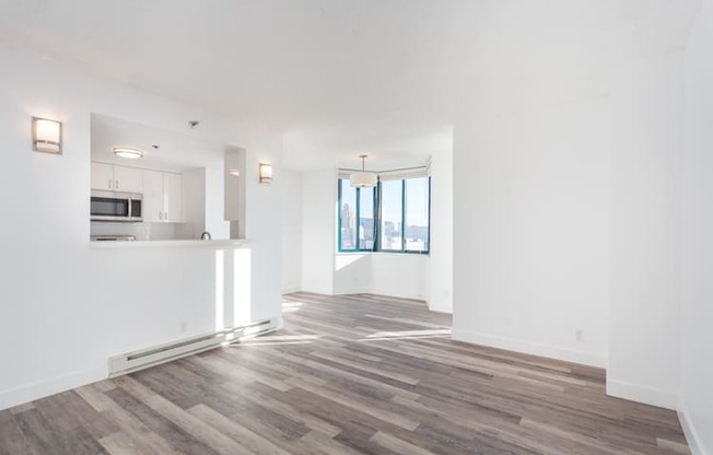 an empty living room with a kitchen in the background