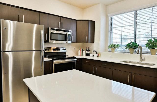 The Highland Kitchen with stainless appliances, dark cabinets, white quartz counters and light faux wood flooring