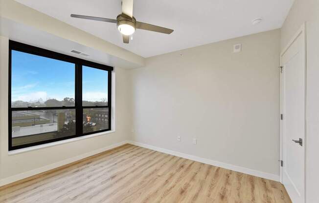 A room with a ceiling fan and a large window overlooking a cityscape.