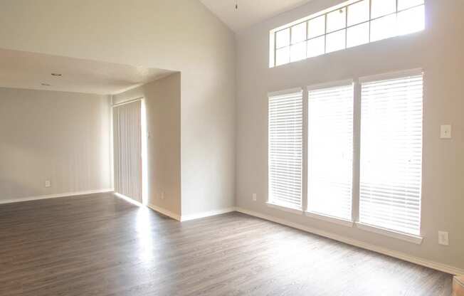 an empty living room with wood floors and large windows at The Broadwater at Salado Creek, San Antonio, Texas