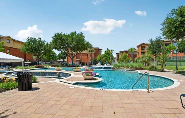 A pool surrounded by a brick patio and trees.