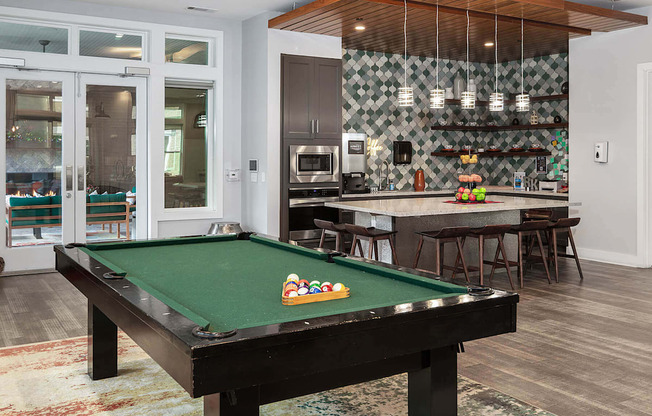 a pool table in a living room with a bar and a kitchen