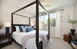 A bedroom with a four poster bed and a window with curtains.