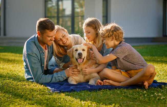 A family of four is sitting on a blanket in the grass with a dog.