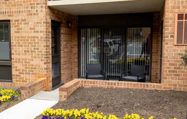 a front porch of a brick building with two chairs and flowers