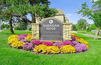 A sign for Sheridan Ridge Townhomes sits in a flower bed.