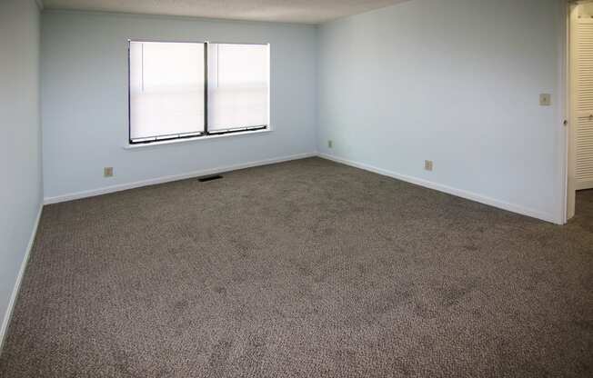 A room with carpeted floor and a window with blinds.