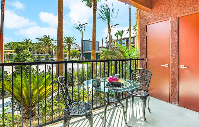 A balcony with a table and chairs overlooking a pool and palm trees.