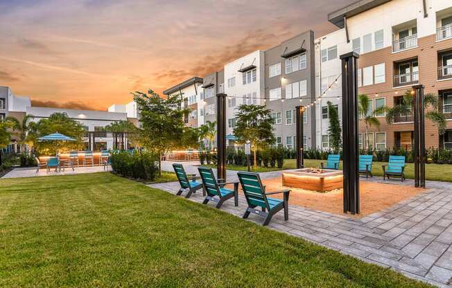 A sunset view of a modern apartment complex with a pool and lounge chairs.