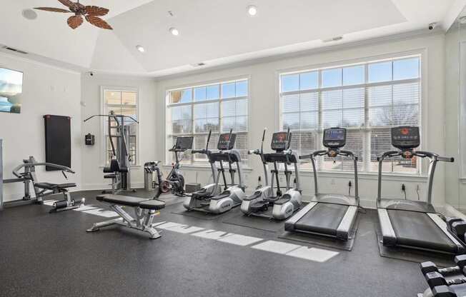 A spacious gym with treadmills, elliptical machines, and a fan.