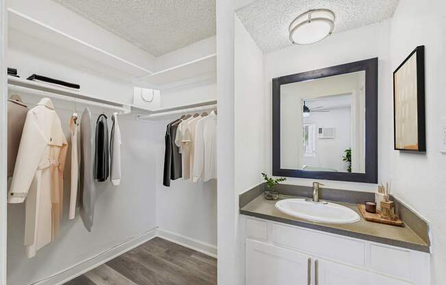 A bathroom with a sink, mirror, and clothes hanging up.