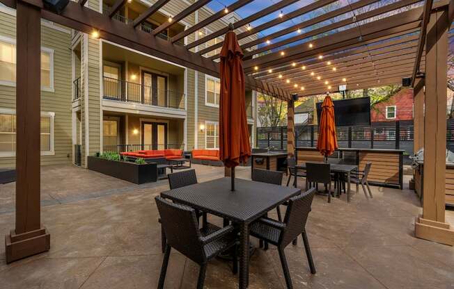 Outdoor lounge at West 39th Street Apartments with pergola, string lights, dining tables, and mounted TV.