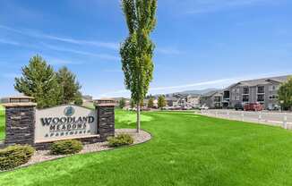 A sign for Woodland Meadows Apartments stands in front of a green lawn.