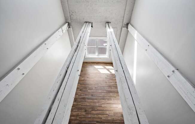 A long wooden staircase with metal handrails on both sides leading to a bright light at the top.