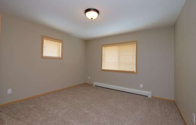 a bedroom with two windows and a carpet. Fargo, ND Urban Plains Apartments