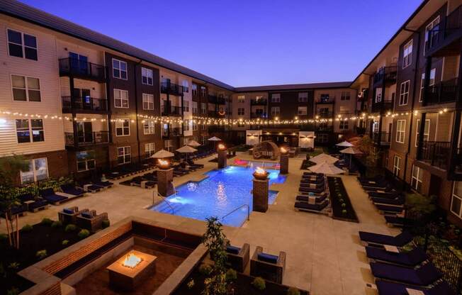 A pool surrounded by lounge chairs and lit string lights.