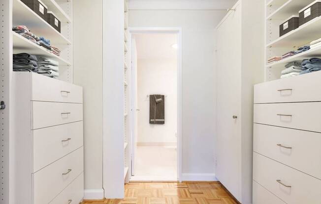 A hallway with white cabinets and drawers on both sides leading to a bathroom.