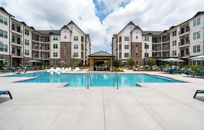 a swimming pool with chaise lounge chairs and umbrellas in front of an apartment building