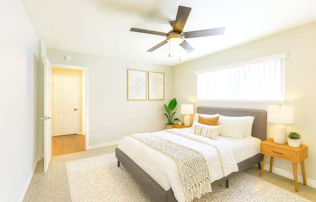 A bedroom with a bed, a ceiling fan, and a nightstand with a plant on it.