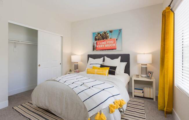 A bedroom with a bed, two lamps, and a yellow curtain.