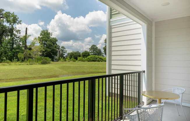 A balcony with a table and chairs overlooking a green field.