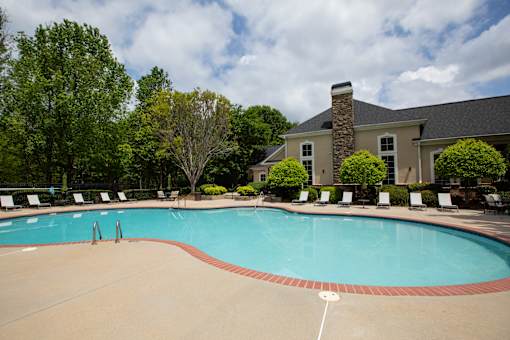 A large swimming pool surrounded by trees and lawn chairs.