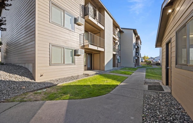 A large sidewalk entering Brix Apartments on a blue sky day. Grass aligns the sidewalk and apartments with balconies. at Brix, Walla Walla, WA, 99362