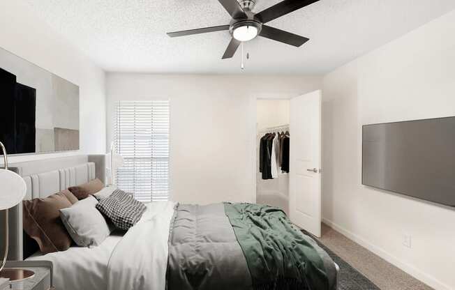 Virtually staged bedroom with carpet, accent rug, wall mounted television, ceiling fan and walk in closet with hanged clothes