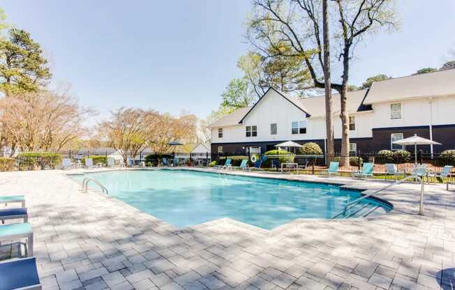 A large swimming pool surrounded by a tiled patio and a white house in the background.