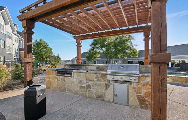 A wooden pergola is over a stone wall with a grill underneath it.