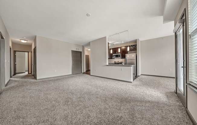 a renovated living room with white walls and carpet and a kitchen